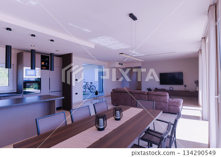 Modern open-plan living and dining room in a luxury villa with large glass doors opening to a private swimming pool, offering a spacious and elegant indoor-outdoor living experience 134290549