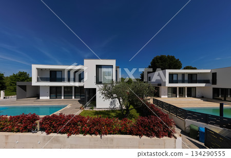 Aerial view of two stunning modern luxury villas with private swimming pools, elegant architecture, and lush green landscaping, set against a beautiful natural backdrop Aerial view of two stunning modern luxury villas with private swimming pools, elegant architecture, and lush green landscaping, set against a beautiful natural backdrop 134290555