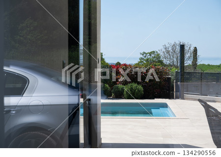 Modern home exterior with swimming pool viewed through glass wall, featuring reflections, minimalist design, landscaped garden, and luxury residential architecture in a serene outdoor setting Modern home exterior with swimming pool viewed through glass wall, featuring reflections, minimalist design, landscaped garden, and luxury residential architecture in a serene outdoor setting 134290556