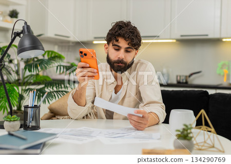 Indian man checking bills on smartphone calculating debt budget numbers worried about money stress 134290769