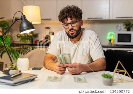 Arabian man counts dollar money cash forms spend save piles plans budget with calculator at night 134290772
