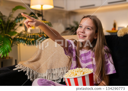 Teenager girl enjoys film eats popcorn laughs loud smiles happy reaction family movie time fun mood Teenager girl enjoys film eats popcorn laughs loud smiles happy reaction family movie time fun mood 134290773