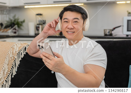 Asian man with wireless headphones enjoys playlist smiles nods to rhythm relaxes with shut eyes calm 134290817