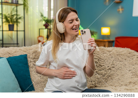 Pregnant woman dances holding smartphone like microphone joyful singing indoors with fun happy vibes 134290888