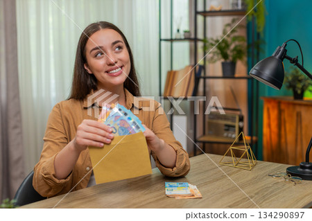 Woman counting euro cash money placing bills into envelope pleased with careful budget planning 134290897