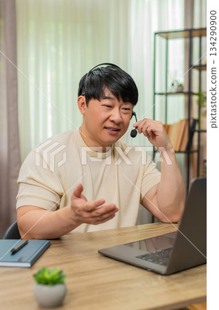 Asian man on laptop headset video call, giving live support with calm tone, online customer service Asian man on laptop headset video call, giving live support with calm tone, online customer service 134290900