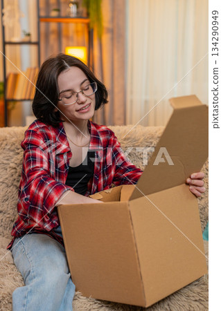 Woman unpacking delivery box at home, smiling with satisfaction while checking new items with joy Woman unpacking delivery box at home, smiling with satisfaction while checking new items with joy 134290949
