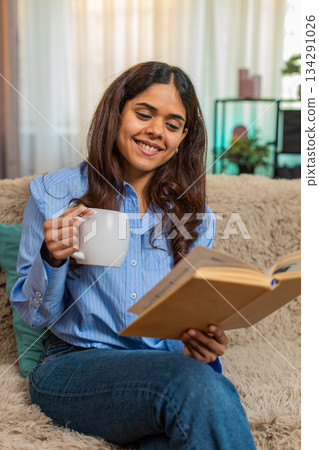 Indian woman drinking coffee and reading book at home enjoying quiet peaceful start of cozy morning Indian woman drinking coffee and reading book at home enjoying quiet peaceful start of cozy morning 134291026
