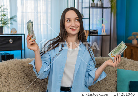 Young woman dancing joyfully on sofa holding cash dollar bills celebrating lottery winning success Young woman dancing joyfully on sofa holding cash dollar bills celebrating lottery winning success 134291040