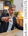 Happy young Caucasian businessman in suit with laptop pointing at camera sitting at home office desk 134291176