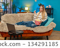 Caucasian woman enjoying movie on sofa eating popcorn laughing watching laptop indoors smiling fun 134291185