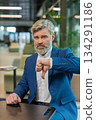 Upset Caucasian businessman in suit showing thumb down sign gesture sitting in modern office lobby 134291186