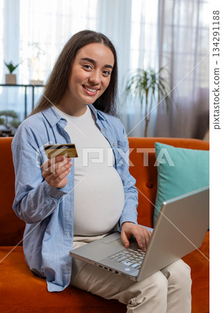 Online shopping buying pregnant woman sitting on home sofa making purchase using laptop credit card 134291188