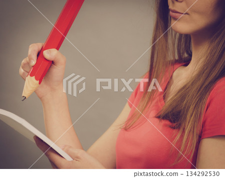 Woman holds huge red pencil and note paper. 134292530
