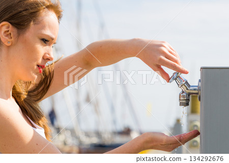Woman drinking water from tap in marina. Woman drinking water from tap in marina. 134292676