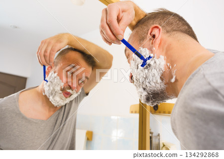 Guy shaving his beard in bathroom Guy shaving his beard in bathroom 134292868