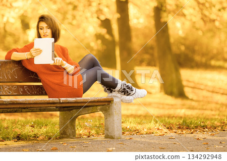 Woman on bench in park with tablet. 134292948