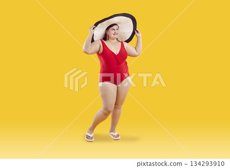 Portrait of cheerful female plus size model wearing beachwear, isolated on orange background. 134293910