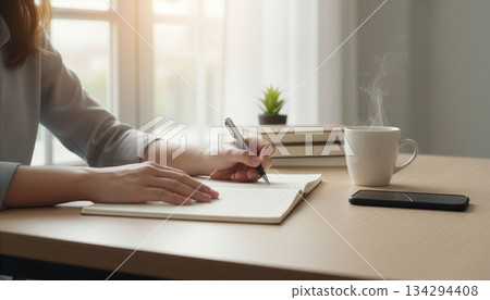 Close-up of a woman's hands writing in a notebook at a table 134294408