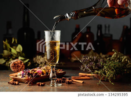 Yellow herbal liquor or mixture is poured from a vintage bottle into a glass. Yellow herbal liquor or mixture is poured from a vintage bottle into a glass. 134295395