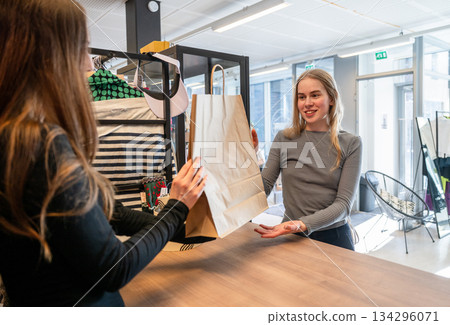 Customer receiving paper bag from shop assistant in secondhand store Customer receiving paper bag from shop assistant in secondhand store 134296071