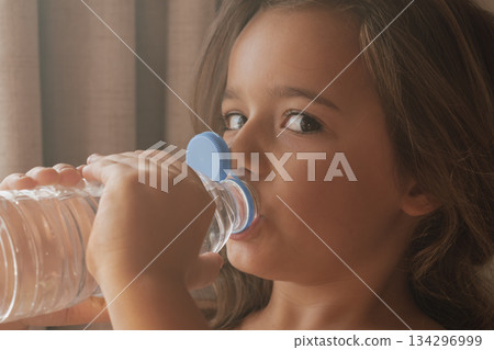Candid close-up: child drinking from a disposable water bottle on a sunny day Candid close-up: child drinking from a disposable water bottle on a sunny day 134296999