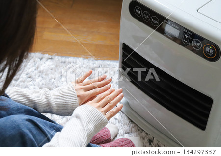 一位女士正在用電風扇暖手。 134297337