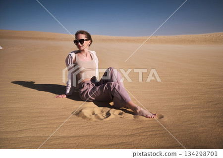 Woman Sitting on Golden Desert Sand Dunes Woman Sitting on Golden Desert Sand Dunes 134298701