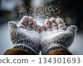 Hands wearing gray mittens catch snowflakes in a winter scene as white snow covers the ground around them 134301693