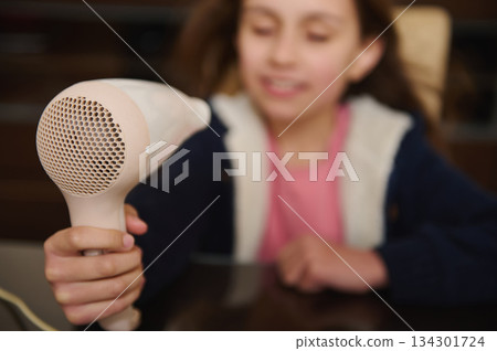 Young Girl With Hair Dryer In Foreground During Home Grooming Session Young Girl With Hair Dryer In Foreground During Home Grooming Session 134301724