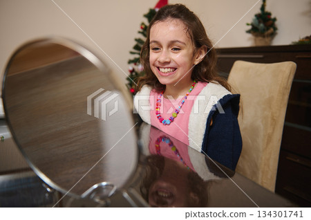 Cheerful Girl Smiling At Vanity Mirror During Christmas Family Moment With Colorful Beads Cheerful Girl Smiling At Vanity Mirror During Christmas Family Moment With Colorful Beads 134301741