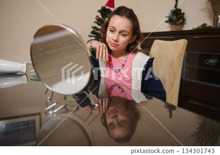 Young Girl Looking Into Mirror At Christmas Table With Jewelry In Cozy Home Setting 134301743