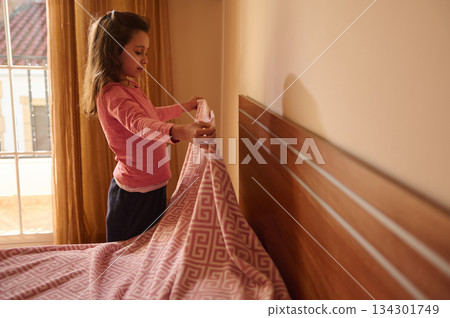 Young Girl Making Bed With Pink Blanket In Bright Sunlit Bedroom 134301749