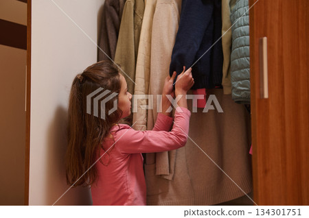 Little Girl Selecting Clothes From Closet With Coats In A Pink Shirt For A Warm Wardrobe Moment 134301751