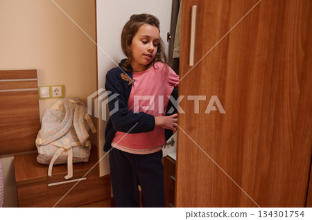 Young Girl In Pink Shirt Explores Open Closet In Cozy Bedroom Young Girl In Pink Shirt Explores Open Closet In Cozy Bedroom 134301754