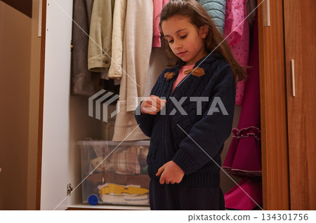 Young Girl Trying On A Navy Knit Sweater In A Closet At Home Young Girl Trying On A Navy Knit Sweater In A Closet At Home 134301756