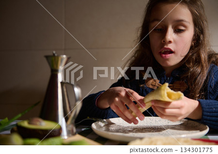 Young Girl Enjoying A Pastry At The Table In A Cozy Kitchen 134301775