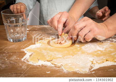 Child and Adult Filling Dough Circles Together for Homemade Patties Child and Adult Filling Dough Circles Together for Homemade Patties 134301902