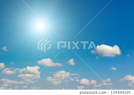 Bright blue sky with radiant sun and scattered cumulus clouds in peaceful daylight atmosphere 134304205