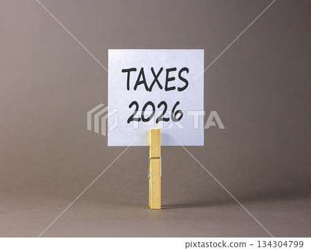 Taxes 2026 new year symbol. Concept words Taxes 2026 on beautiful white paper on wooden clothespin. Beautiful grey background. Business and taxes 2026 new year concept. Copy space. Taxes 2026 new year symbol. Concept words Taxes 2026 on beautiful white paper on wooden clothespin. Beautiful grey background. Business and taxes 2026 new year concept. Copy space. 134304799
