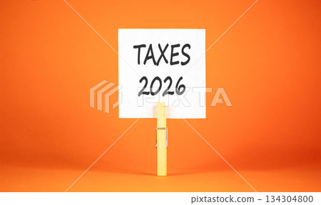 Taxes 2026 new year symbol. Concept words Taxes 2026 on beautiful white paper on wooden clothespin. Beautiful orange background. Business and taxes 2026 new year concept. Copy space. 134304800