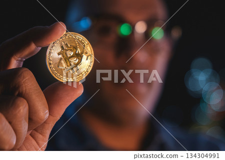 Man holding golden bitcoin coin observing cryptocurrency market Man holding golden bitcoin coin observing cryptocurrency market 134304991