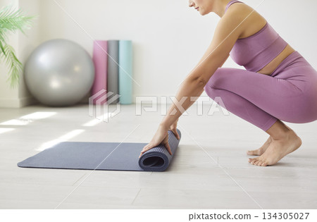 Fit young woman in sportswear rolling out yoga mat on floor and getting ready for workout session. Fit young woman in sportswear rolling out yoga mat on floor and getting ready for workout session. 134305027