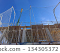 Builders work on a house structure using scaffolding for safety. A construction crane stands nearby, helping lift materials for the ongoing project. 134305372