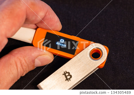 Adult man holding Bitcoin device indoors with neutral expression 134305489