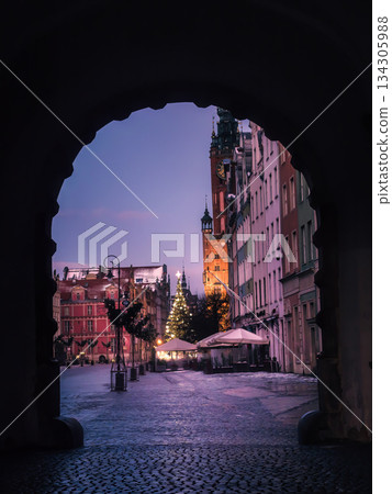 Winter City Square Framed by Archway With Christmas Tree, Historic Clock Tower and Cozy Cafe Lights at Dusk In Old Town, Gdansk, Poland Winter City Square Framed by Archway With Christmas Tree, Historic Clock Tower and Cozy Cafe Lights at Dusk In Old Town, Gdansk, Poland 134305988