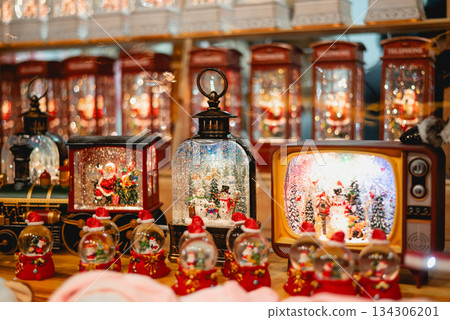 A collection of illuminated Christmas snow globes shaped like a train, TV, and telephone booths at a festive holiday market. A collection of illuminated Christmas snow globes shaped like a train, TV, and telephone booths at a festive holiday market. 134306201