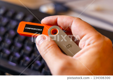 hardware Bitcoin wallet in a hand with compromised message on screen 134306300