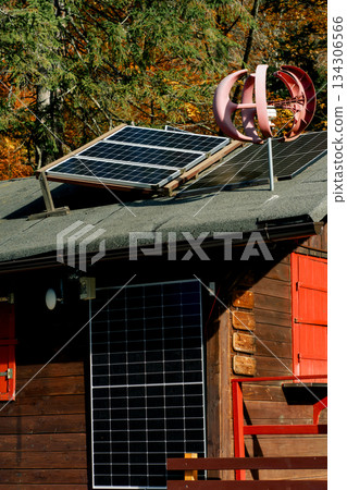 Eco-friendly cabin with solar panels and a small wind turbine generating renewable energy in a scenic autumn forest setting Eco-friendly cabin with solar panels and a small wind turbine generating renewable energy in a scenic autumn forest setting 134306566