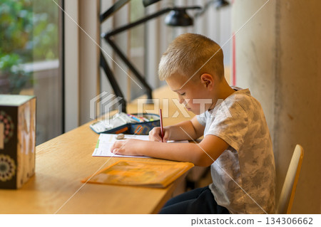 Schoolboy doing homework at a table in the city library. Schoolboy doing homework at a table in the city library. 134306662